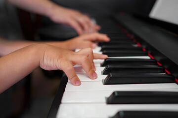 Obraz premium Children's hands and teacher's hands on the piano keys. ?hildren's hands plays the piano, learning a lesson, black and white keys. Training on a synthesizer. Selective focus