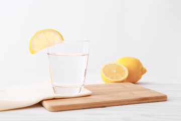 Full glass of transparent water with lemon on wooden table, light background