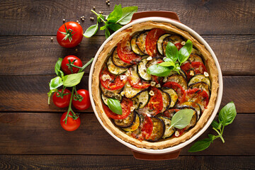 Tart with vegetables. Homemade savory tart with eggplant, zucchini, tomatoes, garlic, mozzarella cheese and fresh basil. Mediterranean  cuisine. View from above - obrazy, fototapety, plakaty
