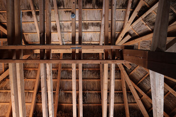View of wooden beams and construction of roof covered by hay from inside the hut