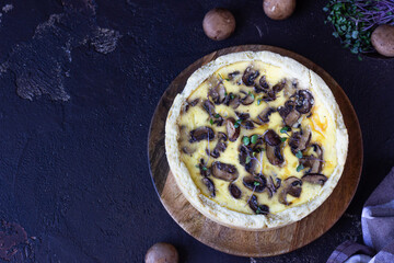Savory tart, pie or quiche with mushrooms and cheese on wooden plate, dark brown textured background. Homemade savory autumn bakery. Top view, copy space.