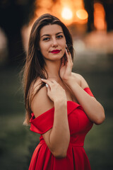 Woman in red dress posing in front of the camera at sunset.