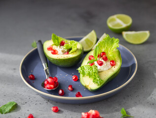 Avocado with pomegranate seeds, ricotta or cream cheese, lettuce leaves and mint on a blue ceramic plate. Healthy organic vegetarian diet food.