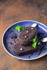 Ice cream popsicle covered with chocolate with mint on a blue ceramic plate. Dark textured background.