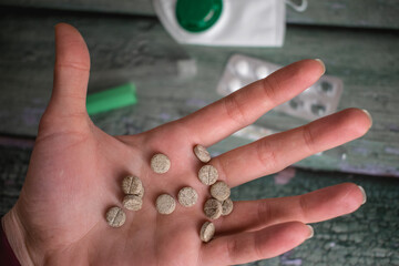 Close up of hand holding pills. Pills, mercury thermometer, medical mask on green wooden background. Medical concept