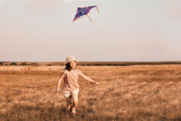 Cute little girl with long hair running with kite in the field on summer sunny day. High quality photo
