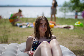 A young girl in a swimsuit sunbathes on the seashore on an air mattress.