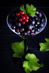Black currant and green leaves on a dark wooden background. Background with currant berries and green leaves. Currant. Close-up