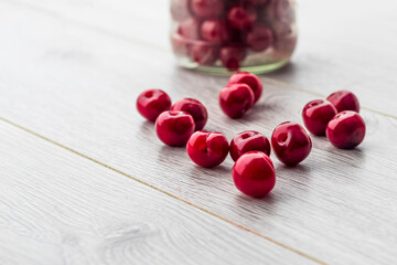 Fresh collected red cherry in a glass jar. Berries are scattered on a wooden background