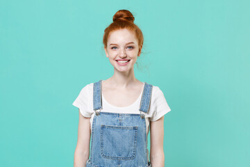 Smiling young readhead girl in casual denim clothes posing isolated on blue turquoise wall background studio portrait. People sincere emotions lifestyle concept. Mock up copy space. Looking camera.