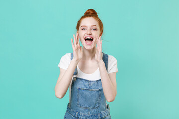 Cheerful young readhead girl in casual denim clothes isolated on blue turquoise wall background studio portrait. People lifestyle concept. Mock up copy space. Screaming with hands gesture near mouth.