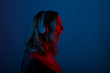 Photo of young woman listening music at headphones with neon lights and screaming