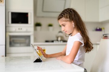 A girl sits at a table in headphones and controls a tablet. Girl smiling