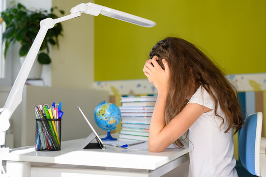 A girl with dark hair is clutching her head with both hands. Girl doing homework