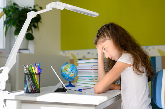 A girl with dark hair is clutching her head with her right hand. The girl does not want to do homework and she is in a bad mood