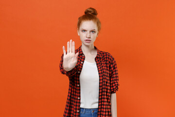 Displeased young readhead girl in casual red checkered shirt posing isolated on orange wall...