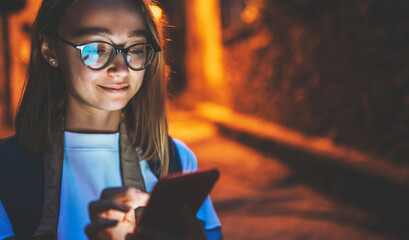 portrait of young blonde girl with cellphone screen reflected in glasses using Internet technology...