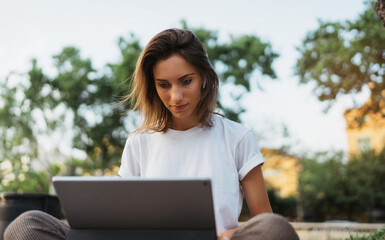 caucasian hipster girl using tablet outdoors, cheerful young freelancer working on touch pad at green park,  female student studying sitting grass with laptop computer outside