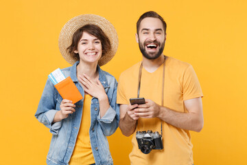 Cheerful tourists couple friends guy girl in summer clothes isolated on yellow background. Passenger traveling abroad on weekends. Air flight journey concept. Hold passport tickets using mobile phone.