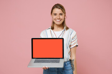 Naklejka premium Smiling young blonde woman girl in casual striped shirt posing isolated on pastel pink background studio. People lifestyle concept. Mock up copy space. Hold laptop pc computer with blank empty screen.