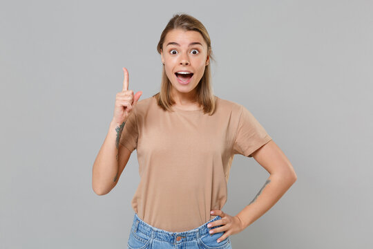 Excited young blonde woman girl in casual beige t-shirt posing isolated on gray background studio portrait. People lifestyle concept. Mock up copy space. Holding index finger up with great new idea.