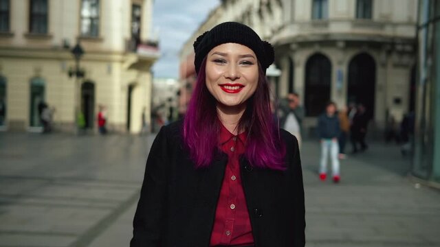 Attractive fashionable young woman walking in a beautiful street. Portrait of elegant asian girl wearing stylish black coat, red shirt, and attractive black cap. Concept of vogue and hipster lifestyle