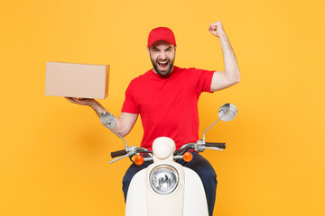 Delivery man in red cap tshirt uniform driving moped motorbike scooter hold cardboard box isolated on yellow background studio Guy employee working courier Service quarantine pandemic covid-19 concept - obrazy, fototapety, plakaty