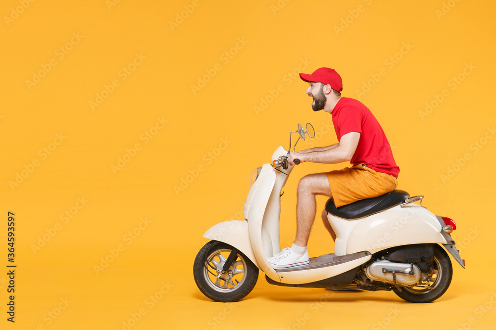 Wall mural delivery man in red cap t-shirt uniform driving moped motorbike scooter isolated on yellow backgroun