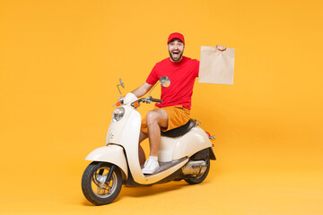 Delivery man in red cap t-shirt uniform driving moped motorbike scooter hold craft paper packet with food isolated on yellow background studio Guy employee working courier Service quarantine concept © ViDi Studio