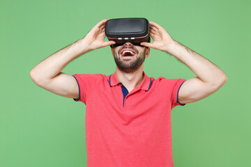 Fototapeta premium Funny young bearded man guy in casual red pink t-shirt posing isolated on green wall background studio portrait. People sincere emotions lifestyle concept. Mock up copy space. Watching in headset.