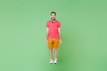 Fototapeta na wymiar full length Excited happy young bearded man guy in casual red pink t-shirt posing isolated on green wall background studio portrait. People lifestyle concept. Mock up copy space. Jumping, having fun.