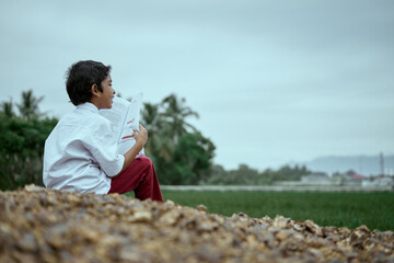 Naklejka na ściany i meble Asian boy wearing school uniform reading and studying outdoor at rice field