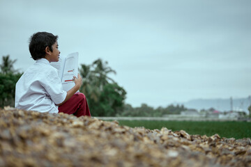 Asian boy wearing school uniform reading and studying outdoor at rice field