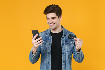 Smiling young man guy in casual denim jacket posing isolated on yellow background studio portrait....