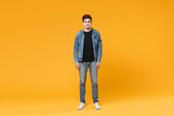 Naklejka premium full length Attractive young man guy 20s in casual denim clothes posing isolated on yellow wall background studio portrait. People sincere emotions lifestyle concept. Mock up copy space. Look camera.
