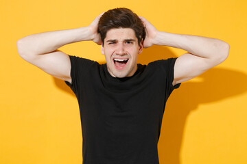 Fototapeta na wymiar Preoccupied worried young man guy in casual black t-shirt posing isolated on yellow wall background studio portrait. People sincere emotions lifestyle concept. Mock up copy space. Put hands on head.