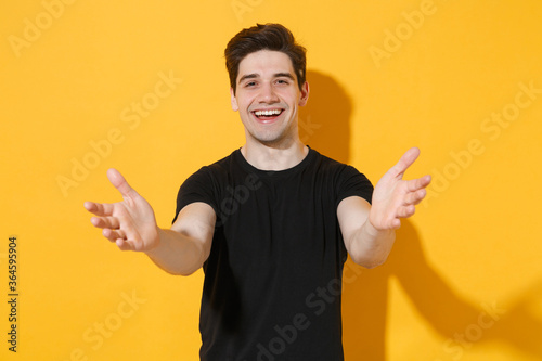 Joyful Young Man Guy s Wearing Casual Black T Shirt Posing Isolated On Yellow Background Studio Portrait People Lifestyle Concept Mock Up Copy Space Standing With Outstretched Hands For Hugs Wall Mural Vidi