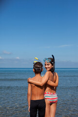 Brother and sister wearing snorkels and hugging on beach