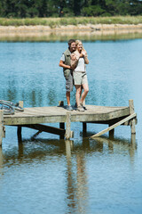 Fototapeta na wymiar Smiling couple hugging on dock over lake