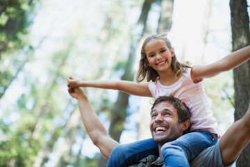 Father carrying daughter on shoulders in woods