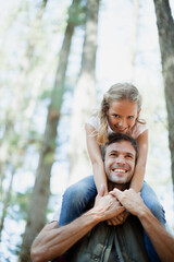 Smiling father carrying daughter on shoulders in woods