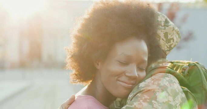 Cloe up of young happy African American couple in love meeting and hugging outdoors at street. Handsome man soldier coming back and embracing girlfriend. Militarian guy returning from army to girl.