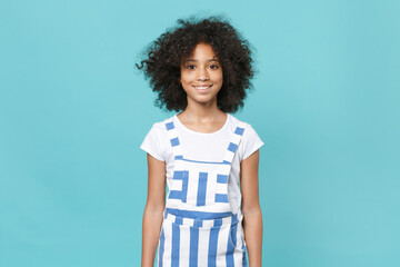 Smiling little african american kid girl 12-13 years old in casual striped clothes isolated on blue background children studio portrait. Childhood lifestyle concept. Mock up copy space Looking camera.