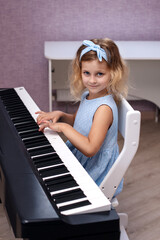 a charming six year old blonde girl in a blue dress plays the piano in her bedroom