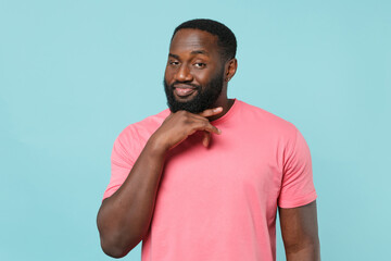 Smiling young african american man guy in casual pink t-shirt posing isolated on blue wall background studio portrait. People emotions lifestyle concept. Mock up copy space. Put hand prop up on chin.