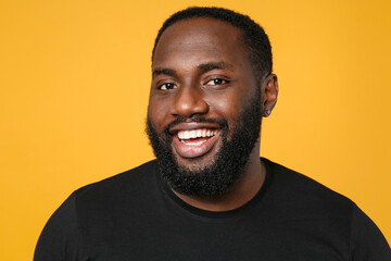 Close up of smiling cheerful african american man football fan in casual black t-shirt isolated on yellow background studio portrait. People lifestyle concept. Mock up copy space. Looking camera.