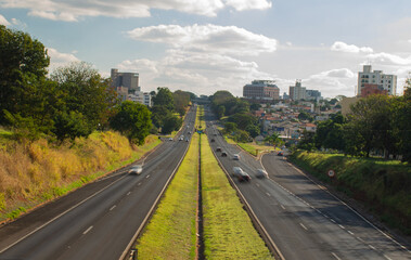 A road crossing a Brazilian city with cars in motion on a sunny afternoon, showcasing urban life and transportation in a vibrant setting