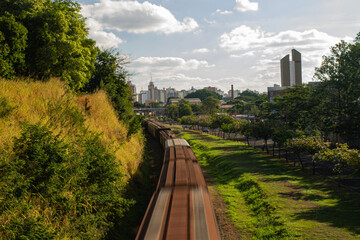 Obraz premium A freight train passing through the city of São José do Rio Preto, SP, during sunset, highlighting transportation and urban scenery with warm golden light.