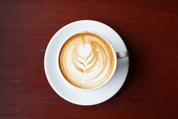 Hot latte with heart latte art in a cup with a white plate on the brown wood table.