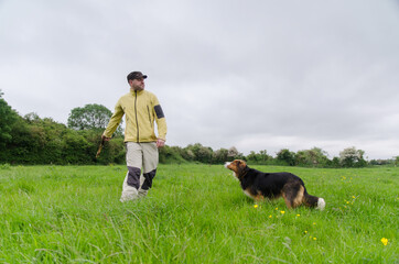 adult man throws a stick to a dog on a green field